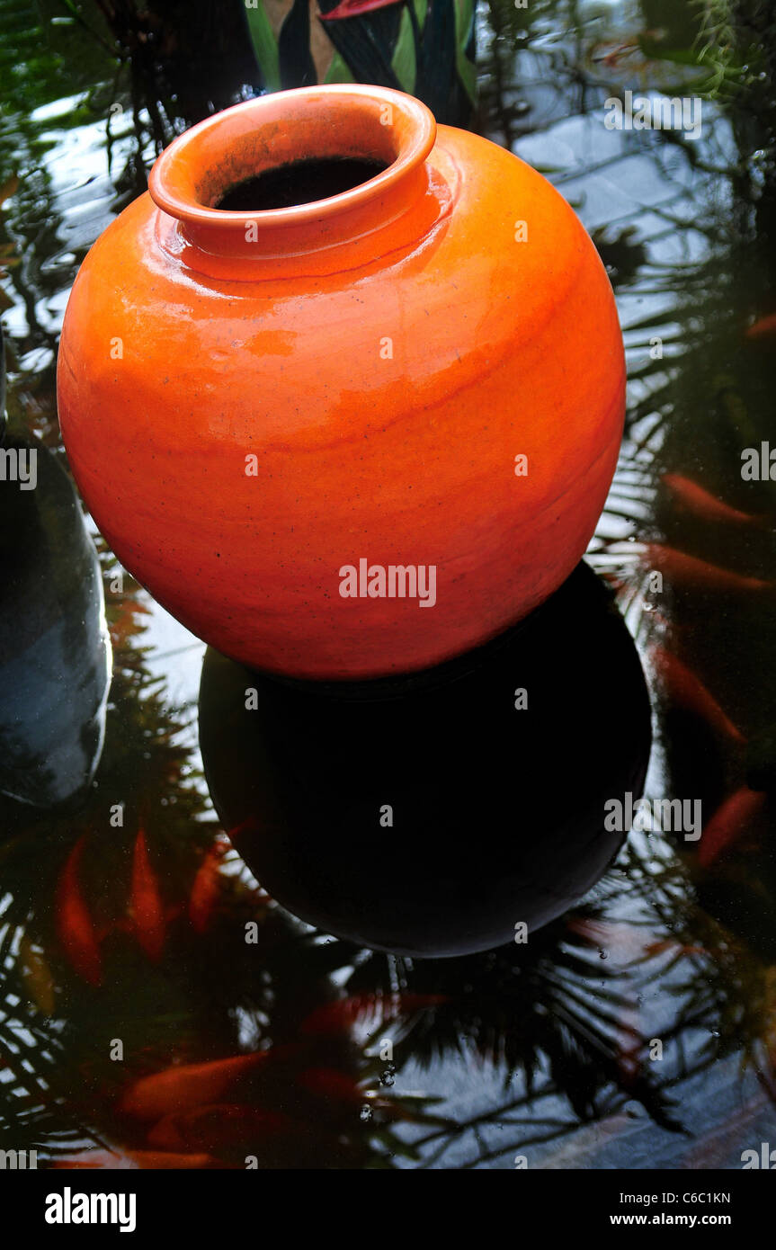 Orange colored terracotta pot between water plants in a water ditch