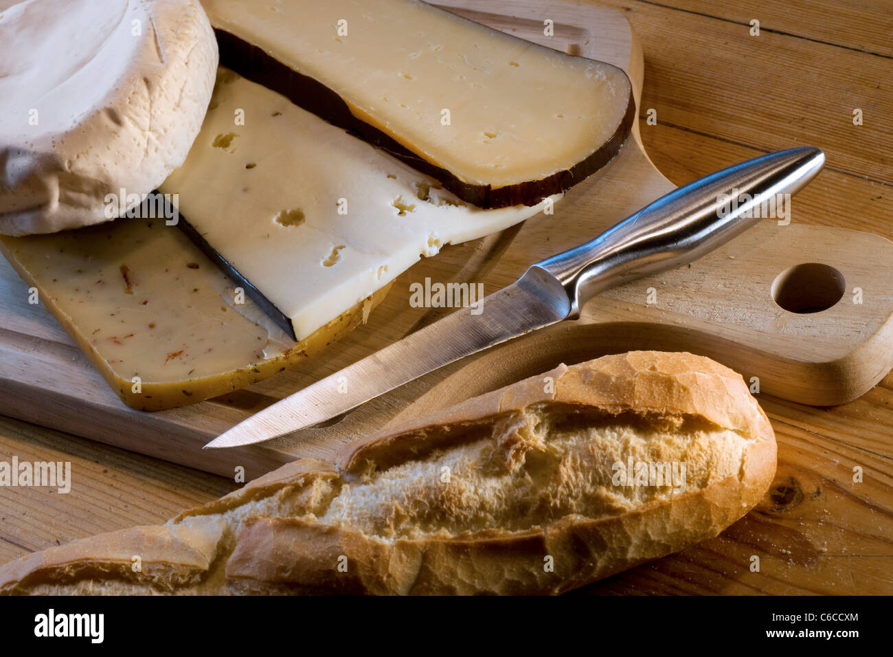 Assortment of cheeses, bread and knife on wooden cheeseboard Stock Photo