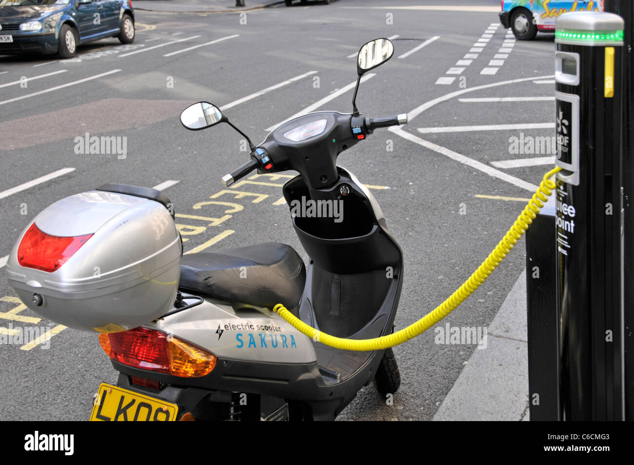 Electric car charging station & recharging parking bay occupied by scooter battery connected to electricity pillar yellow cable street scene London UK Stock Photo