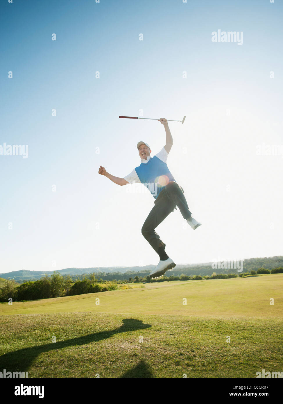 Excited Caucasian golfer jumping in mid-air on golf course Stock Photo