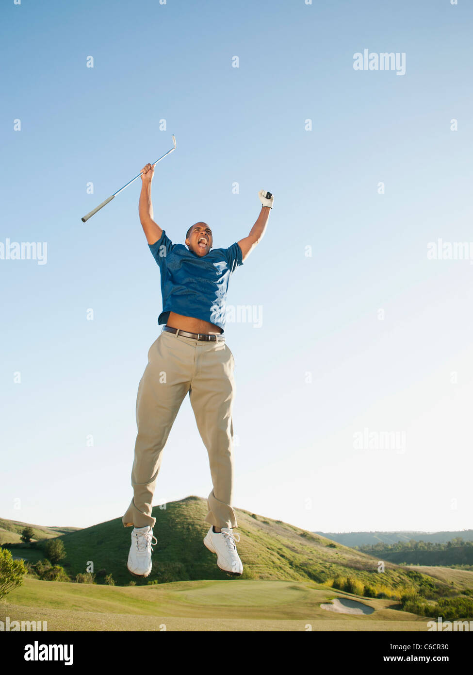 Excited Black golfer jumping in mid-air on golf course Stock Photo