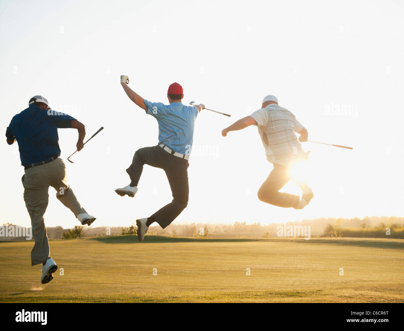 Excited golfers jumping in mid-air on golf course Stock Photo
