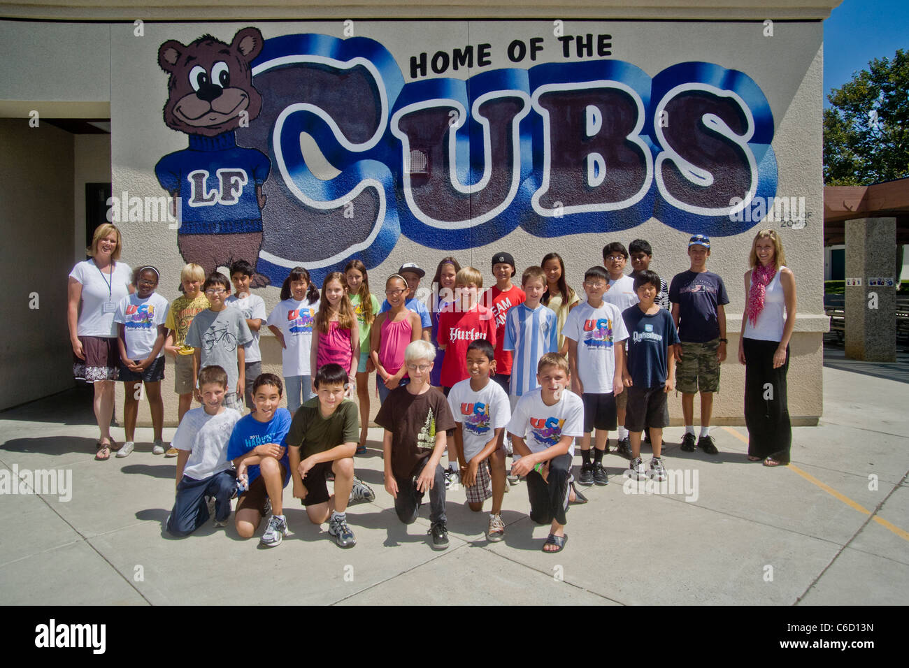 A happy group of students in a college-sponsored summer learning project pose for a group photo before a mural at a local school Stock Photo