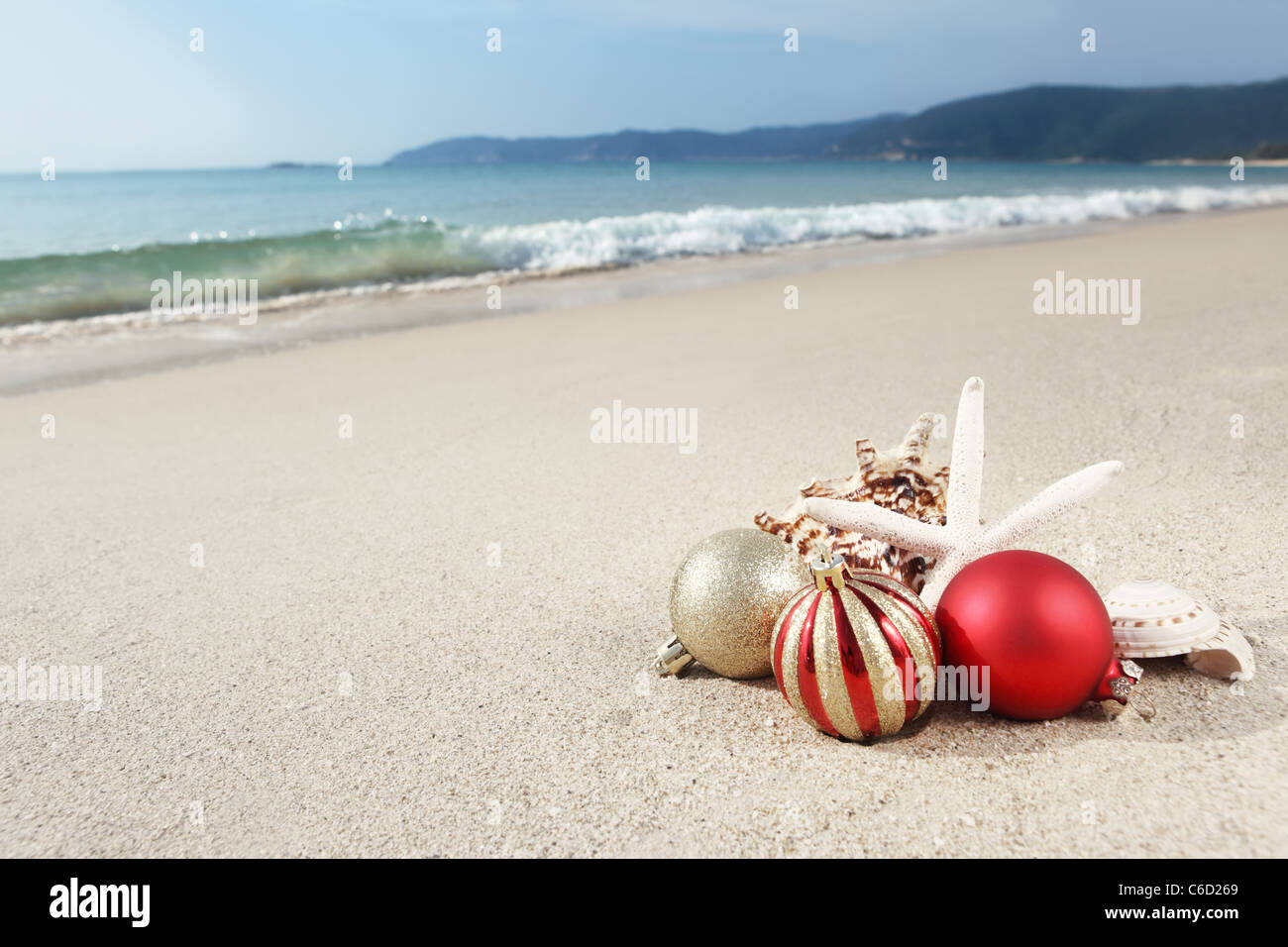 Christmas balls and seashells on the beach near the sea. Stock Photo