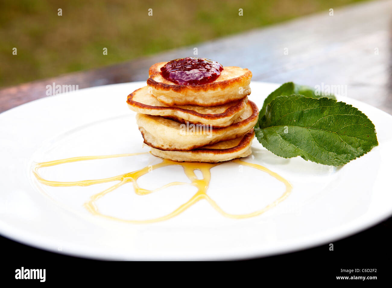 Pancakes On A Plate Covered With Jam And Maple Syrup With Mint On The Side Stock Photo