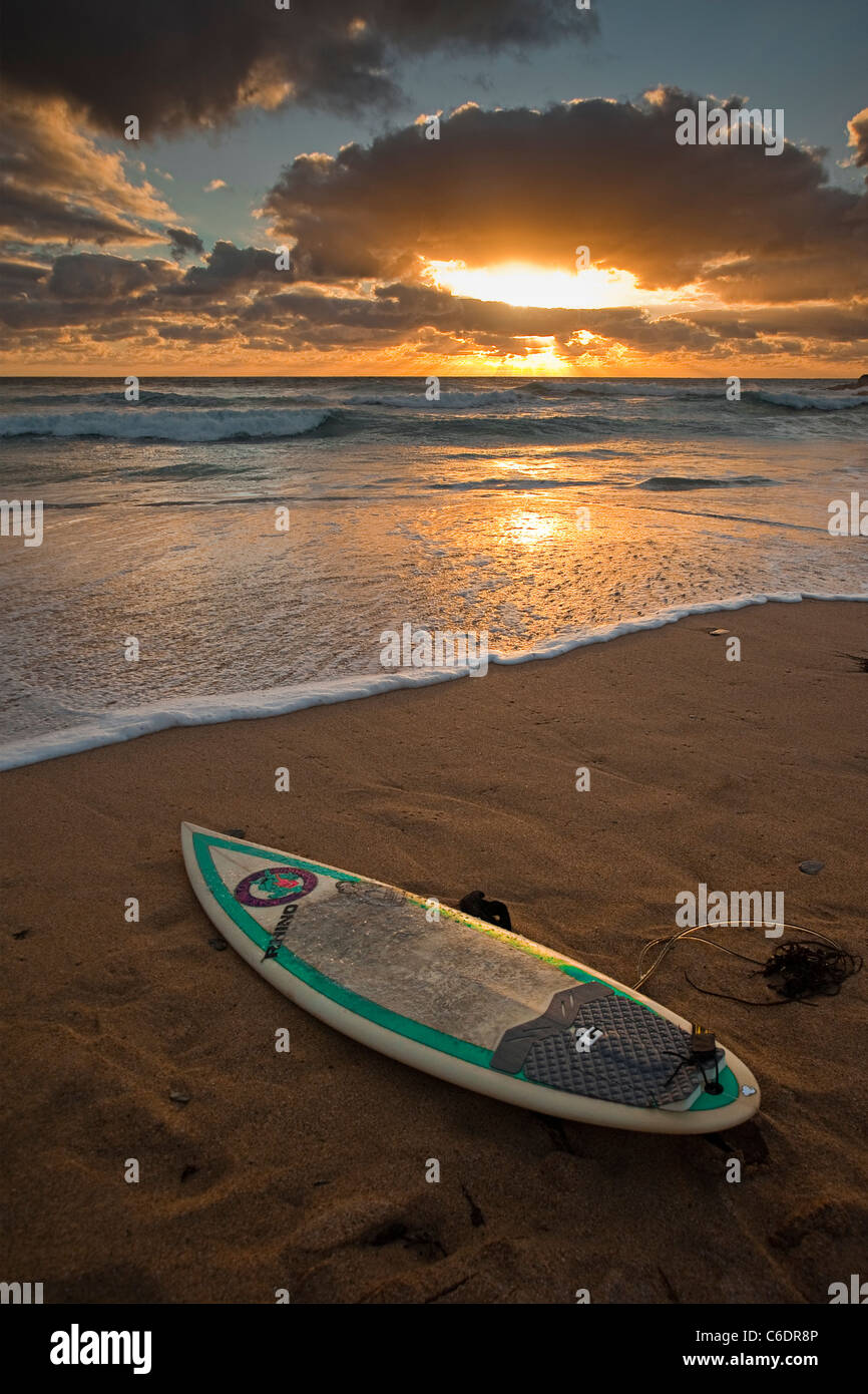 A lone surf board on a beach during a dramatic sunset at Constantine Bay Newquay England Stock Photo