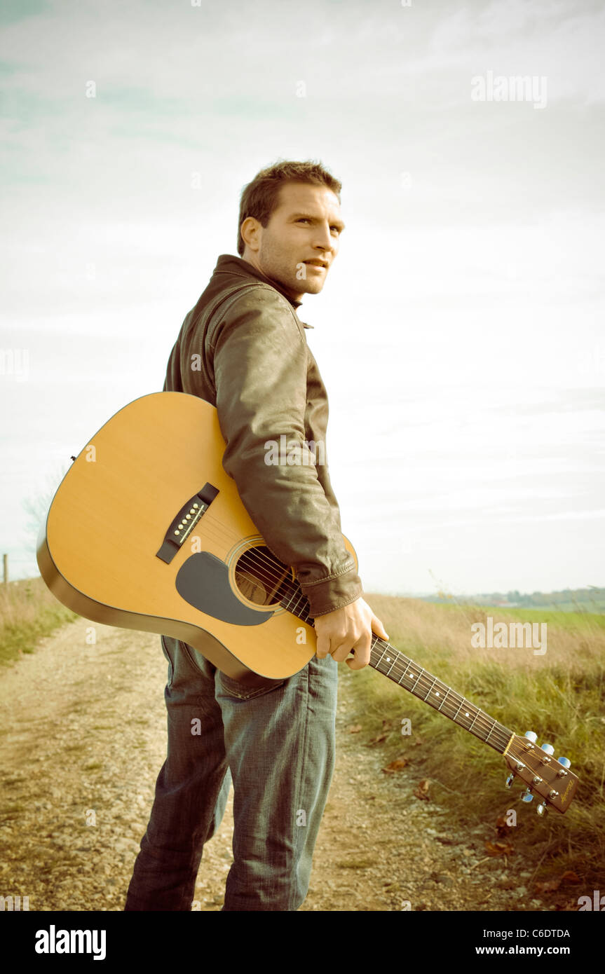 Man with a guitar walking along a road Stock Photo