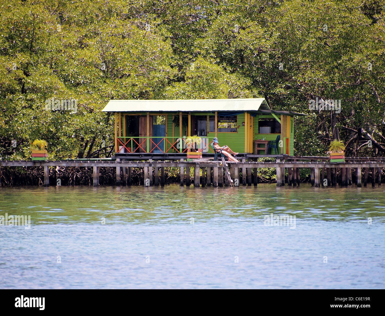 Tropical bungalow over water with people resting on the dock and luxuriant mangrove trees in background, Caribbean sea, Bocas del Toro, Panama, Centra Stock Photo
