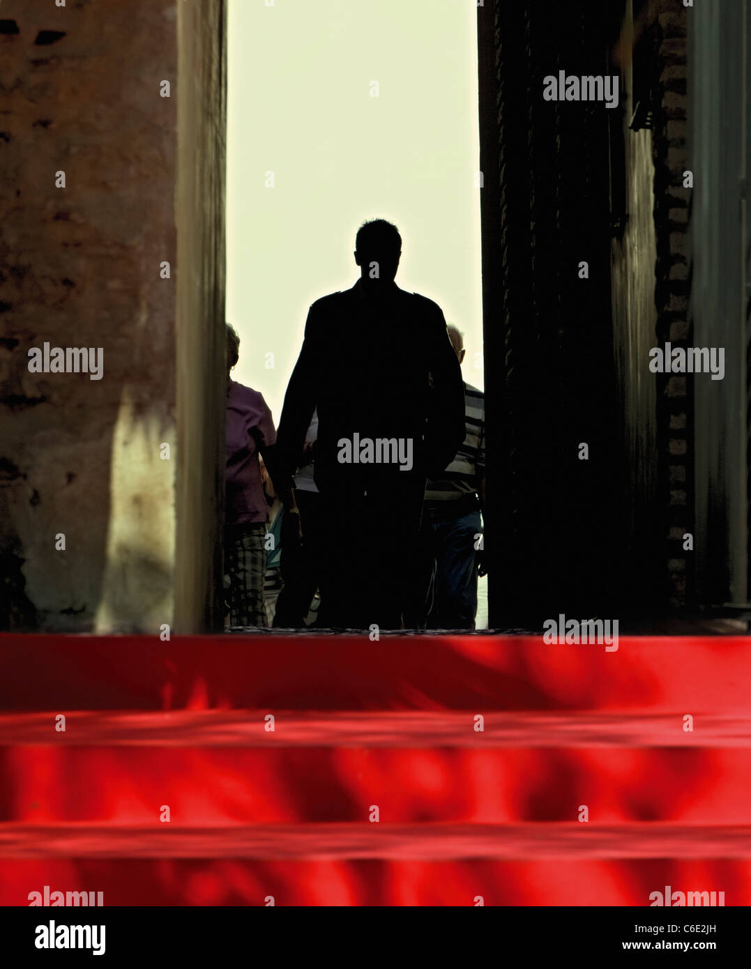 Silhouetted figures walking on a red carpet. Stock Photo