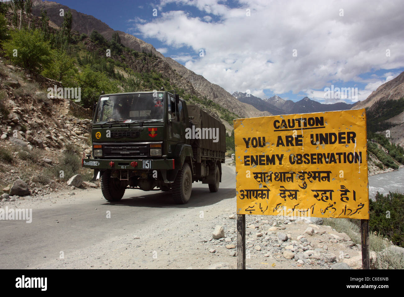 Indian army truck passes warning sign on the hazardous road to Kargil close to Pakistan border. Jammu Kashmir, Northern India Stock Photo