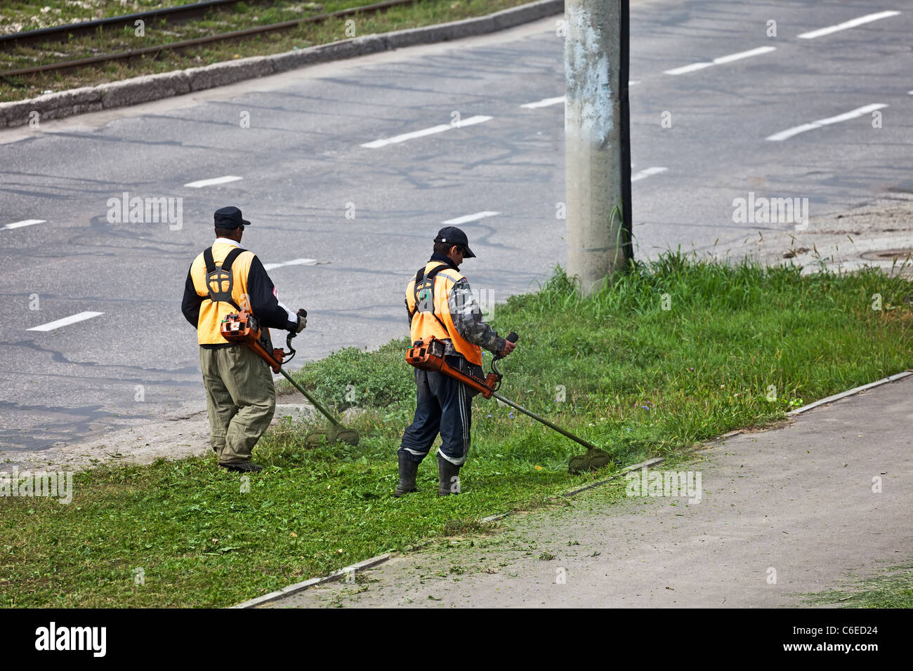 Men with lawn mower triming grass near a road. Stock Photo