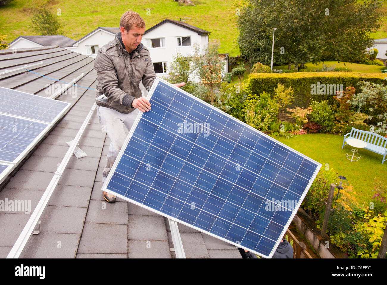 Technicians fitting solar photo voltaic panels to a house roof in Ambleside, Cumbria, UK. Stock Photo