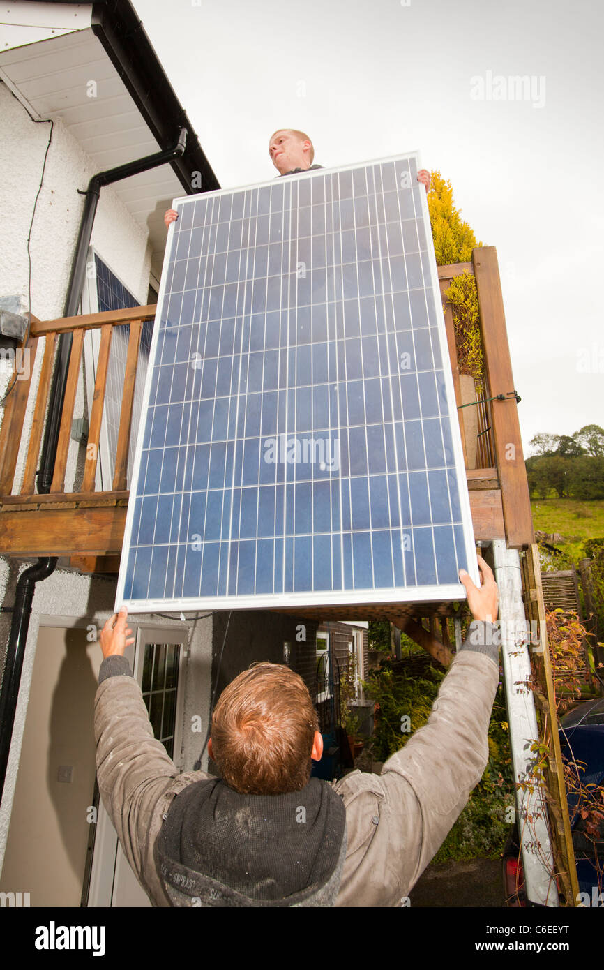 A technician fitting solar photo voltaic panels to a house roof in Ambleside, Cumbria, UK. Stock Photo