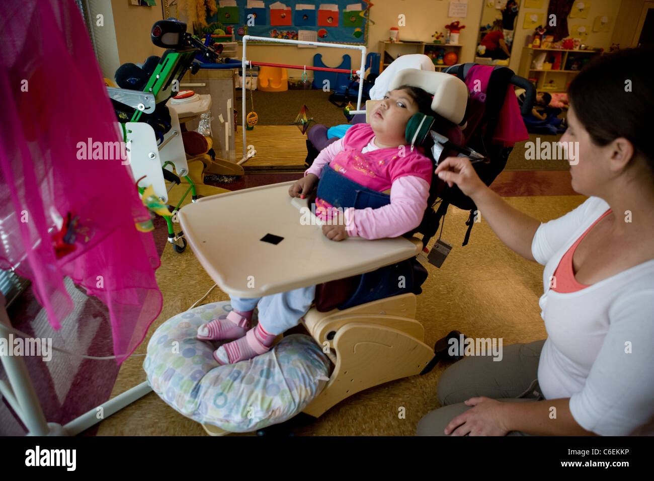 Speech therapist works with seven year old Hispanic non-verbal girl on using head switch to turn on a fan. Stock Photo