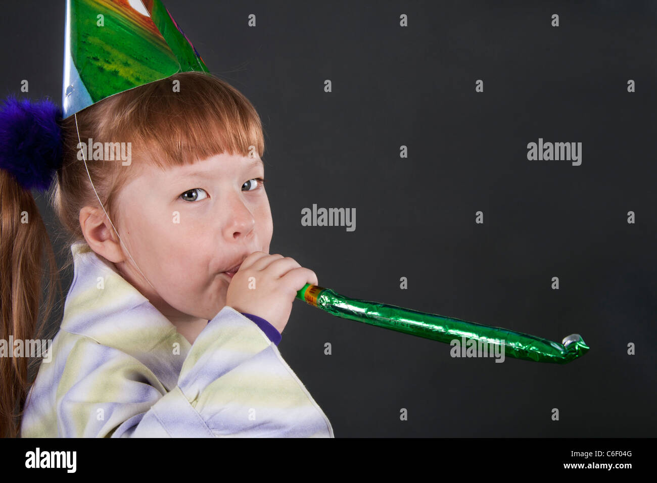 Horizontal view of little girl playfully blowing noisemakers a birthday