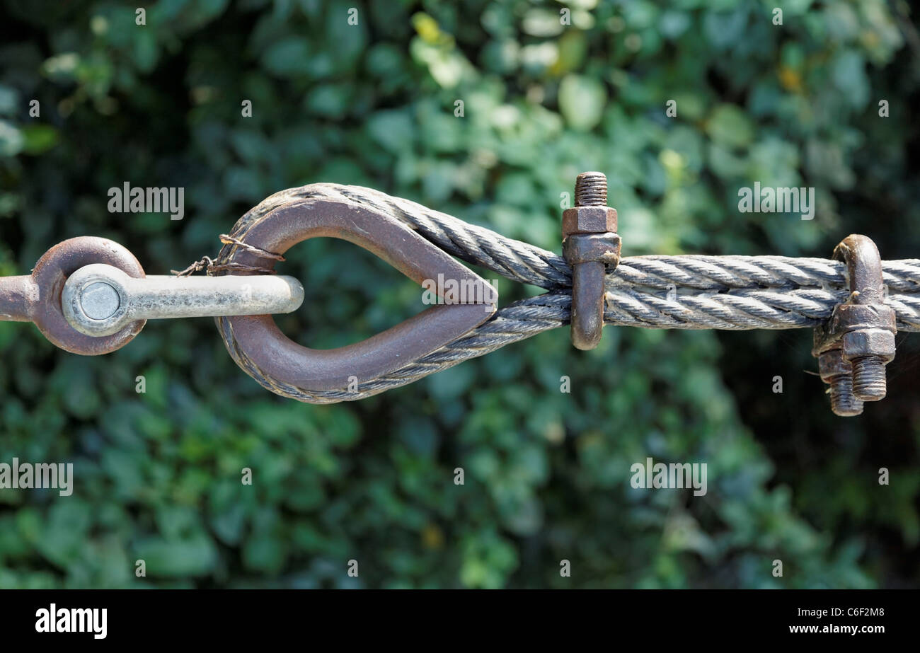 Rusty greased steel wire cable rope clamped around an eyelet with rusty U bolts linked to a galvanized clasp, structural support Stock Photo