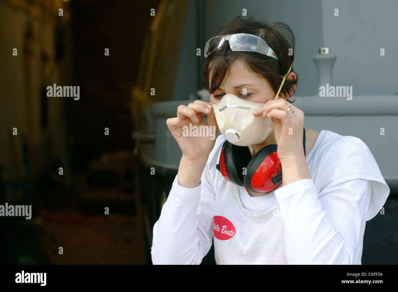 A young woman putting on a face mask, ear defenders and safety goggles for protection whilst working. Stock Photo
