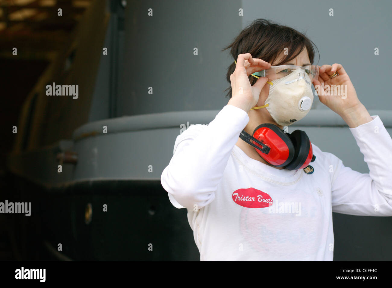 A young woman putting on a face mask, ear defenders and safety goggles for protection whilst working. Stock Photo