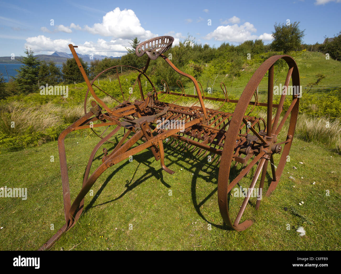 Rusty old Lion Trip Action Rake farm machinery made by Bamfords Ltd, in field near Ord, Isle of Skye, Scotland, UK Stock Photo