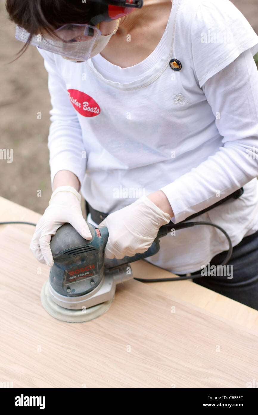 A woman sanding a wooden door at trestles, wearing ear defenders