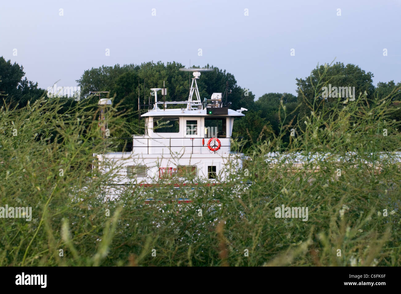 Tugboat on banks of Mississippi River seen through tall grass with trees in background Stock Photo