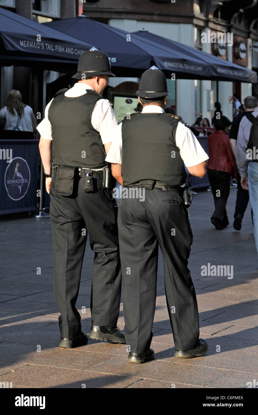 London street scene back view of two Metropolitan Police officers in uniform on a beat patrol in sunny summer Leicester Square West End England UK Stock Photo
