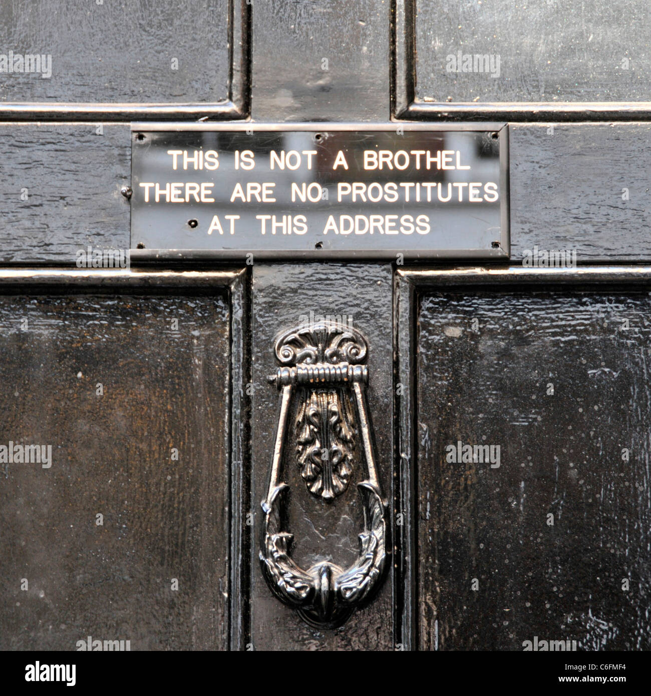 Close up black front door unusual sign in Soho explains premises not a brothel presumably because of nuisance caller using knocker West End London UK Stock Photo