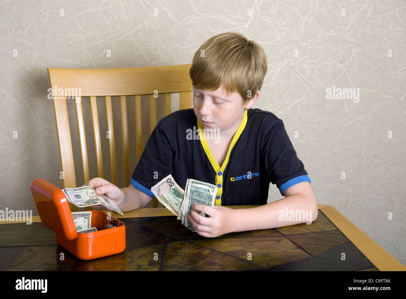 A 12 year old boy is seen counting American Dollars into a small lockable 'cash box' Stock Photo