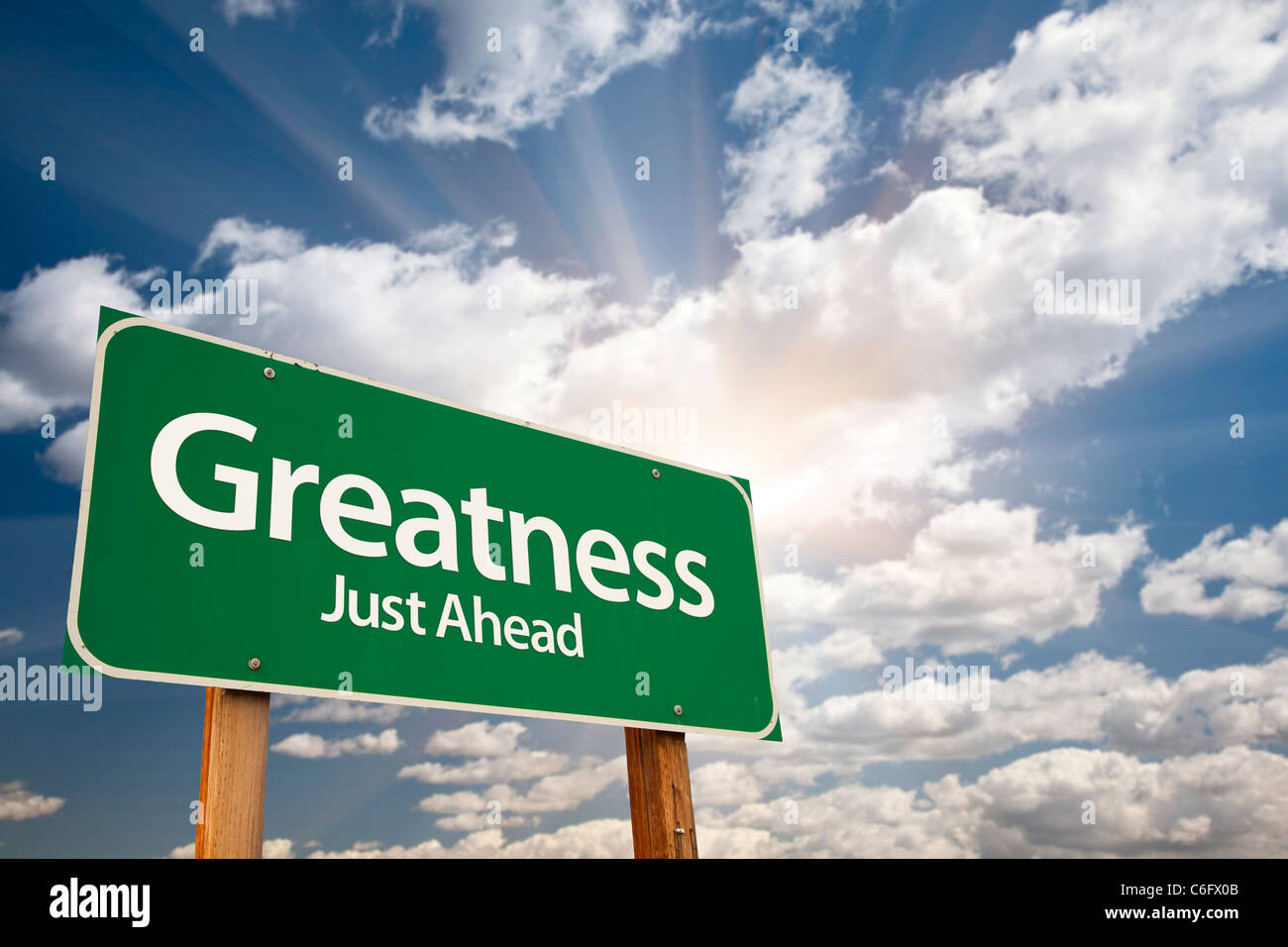 Greatness, Just Ahead Green Road Sign Over Dramatic Sky, Clouds and Sunburst. Stock Photo