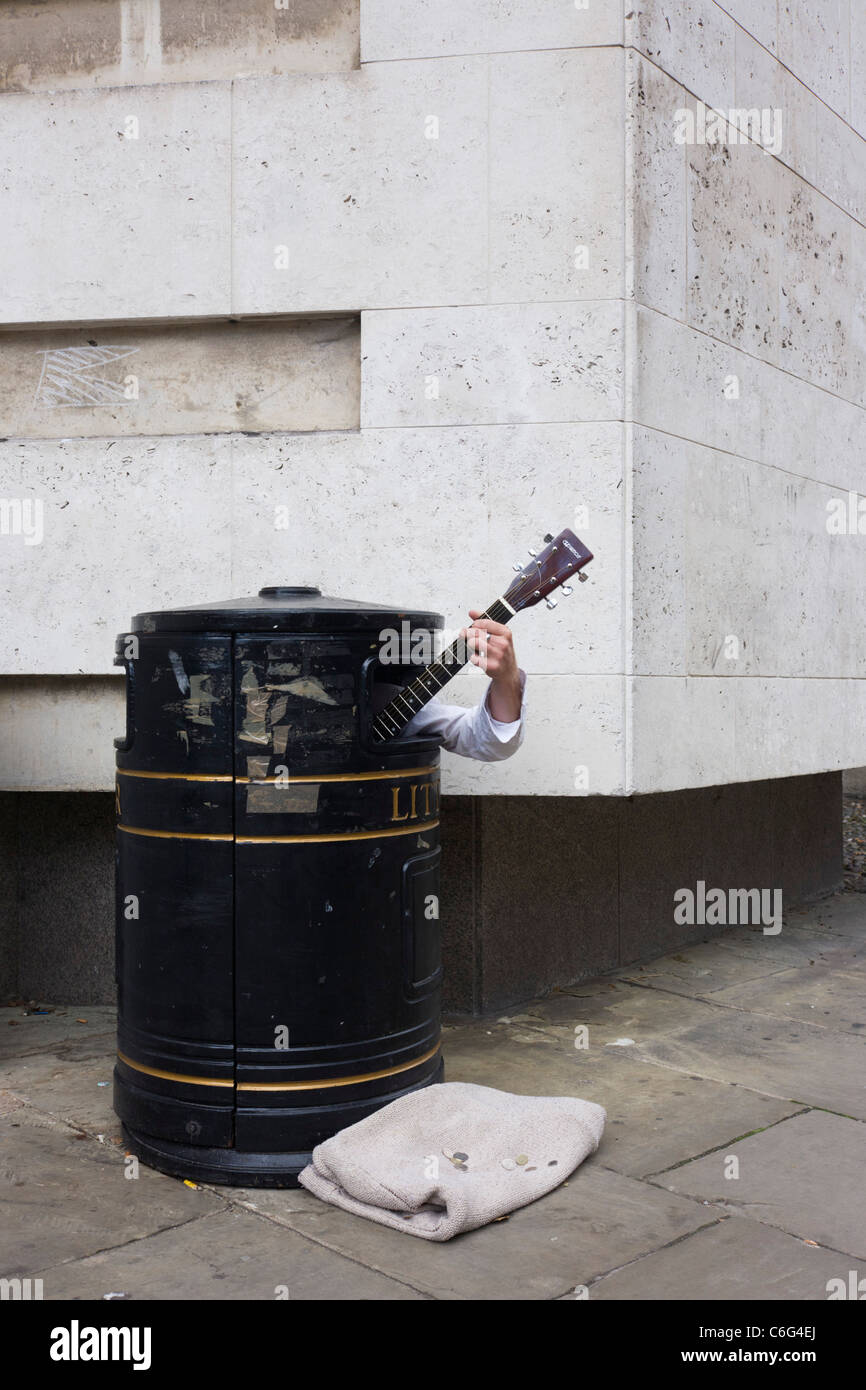 A street busker hides in a litter bin to earn extra cash as passers-by ...