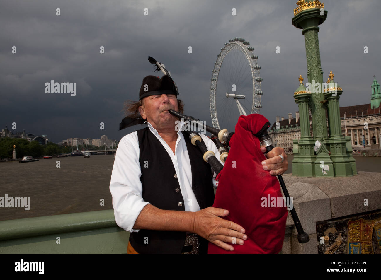 A man plays the bagpipes on Westminster Bridge, the London Eye is visible in the background. Stock Photo