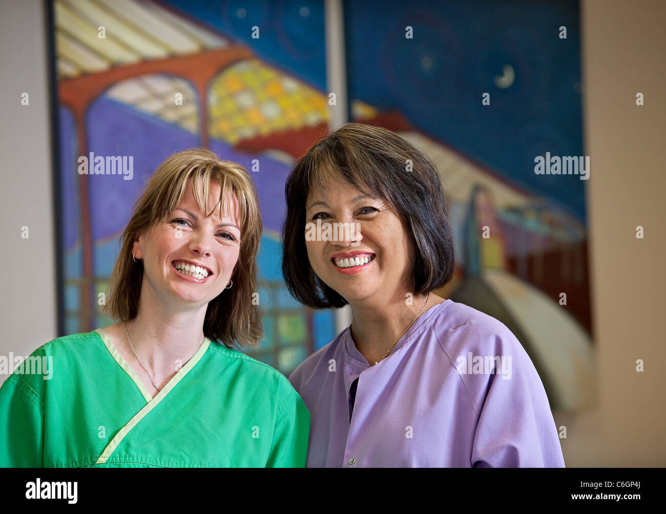 Two nurses pose by a painting in a hospital. Stock Photo