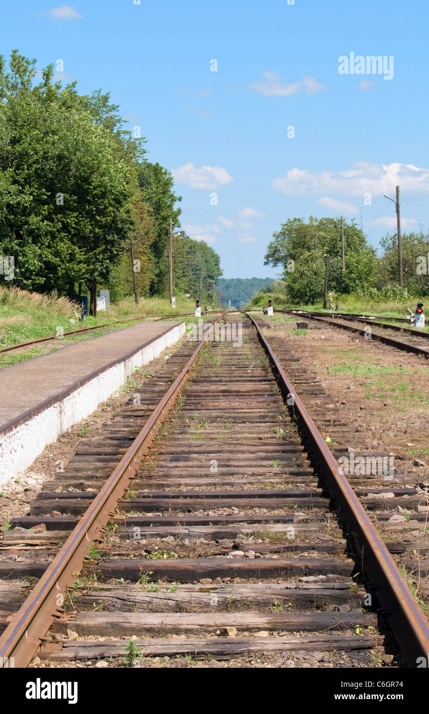 curve in the railway tracks as they disappear between some green trees under blue sky Stock Photo