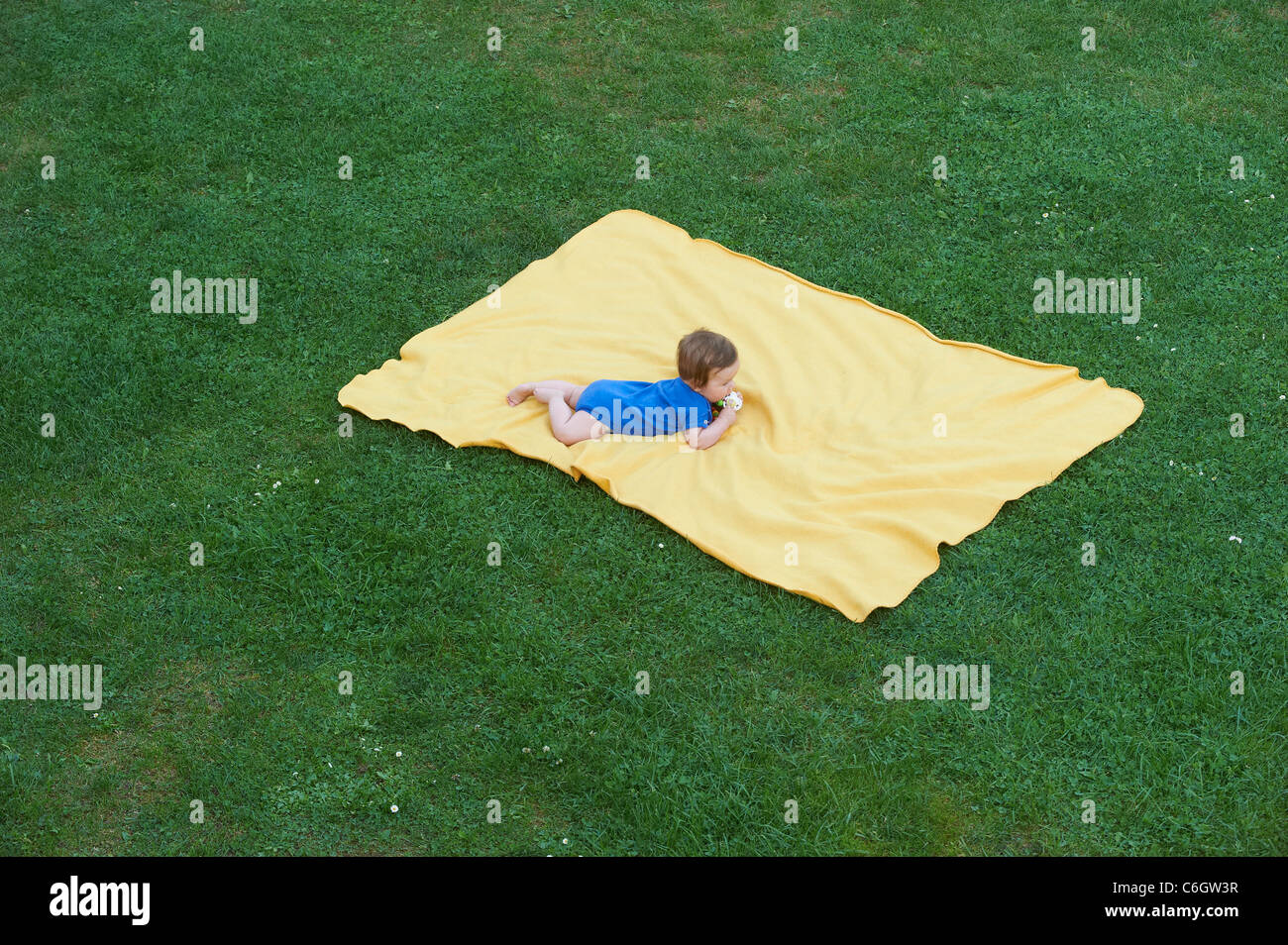 Portrait of little child baby girl lying on yellow blanket in green