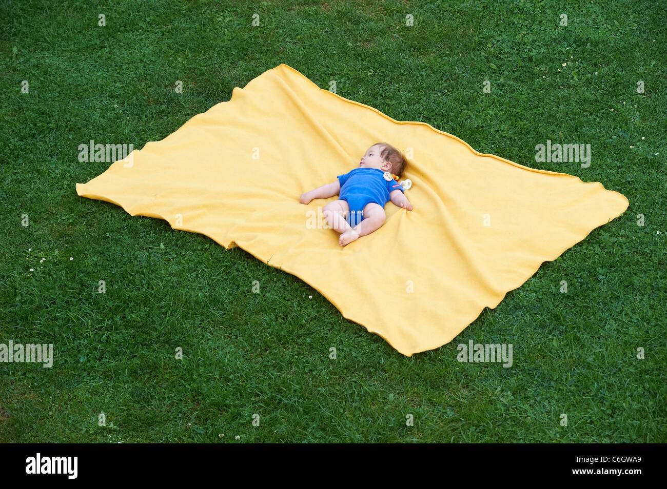 Portrait of little child baby girl lying on yellow blanket in green