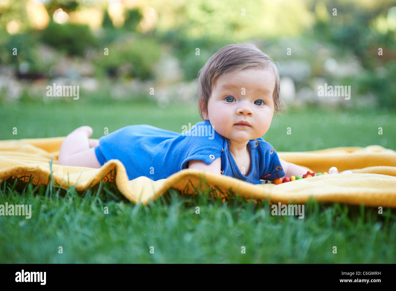 Portrait of little child baby girl lying on yellow blanket in green
