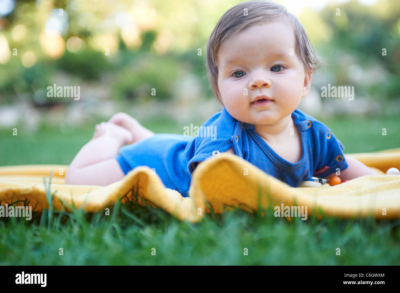 Portrait of little child baby girl lying on yellow blanket in green