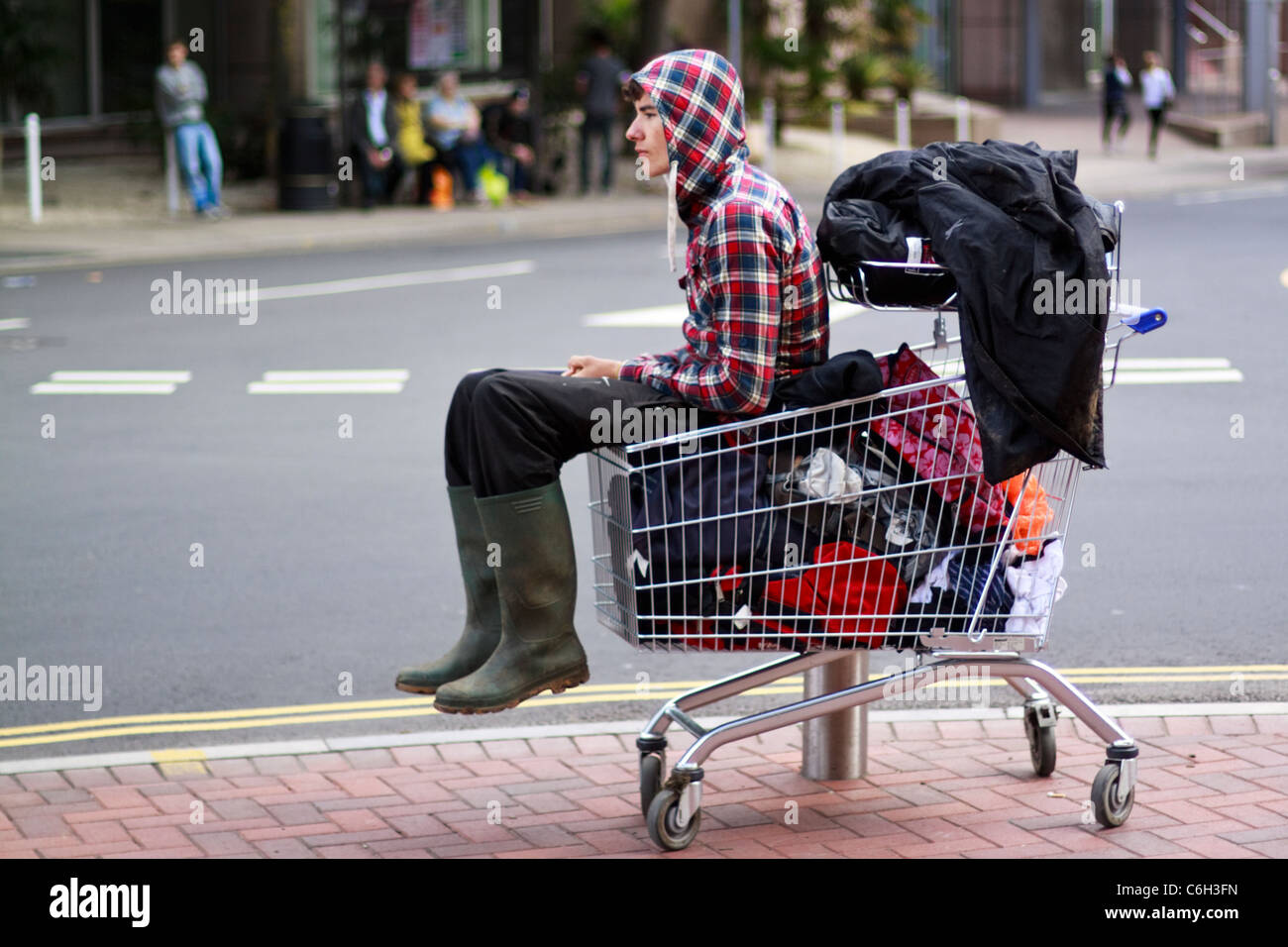 A festival-goer sits in a shopping trolley with all his baggage waiting to go home after Reading Festival 2011 Stock Photo