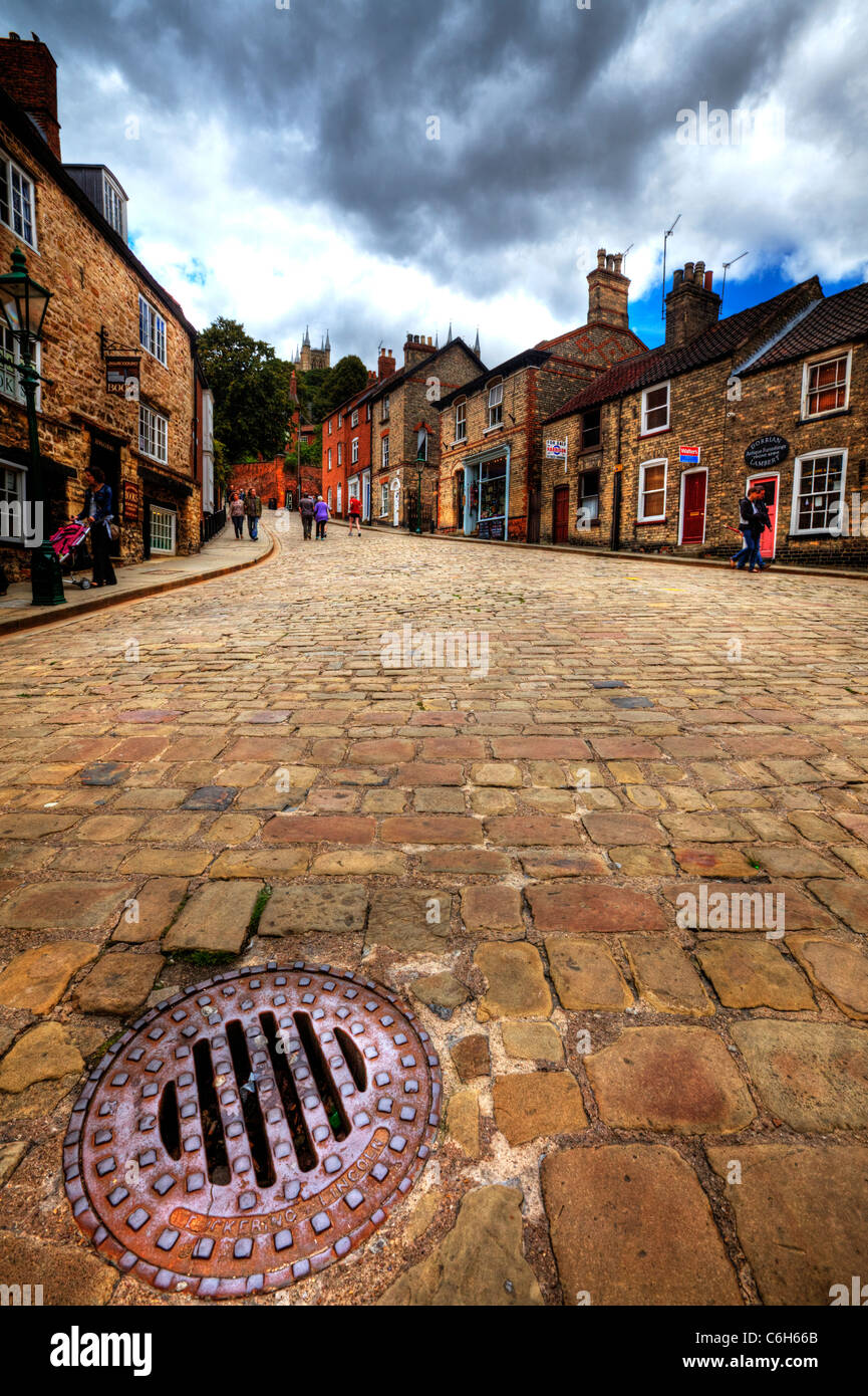 Lincoln City Center, Lincolnshire, England drain cover with the cathedral up steep hill on cobbled street road Stock Photo