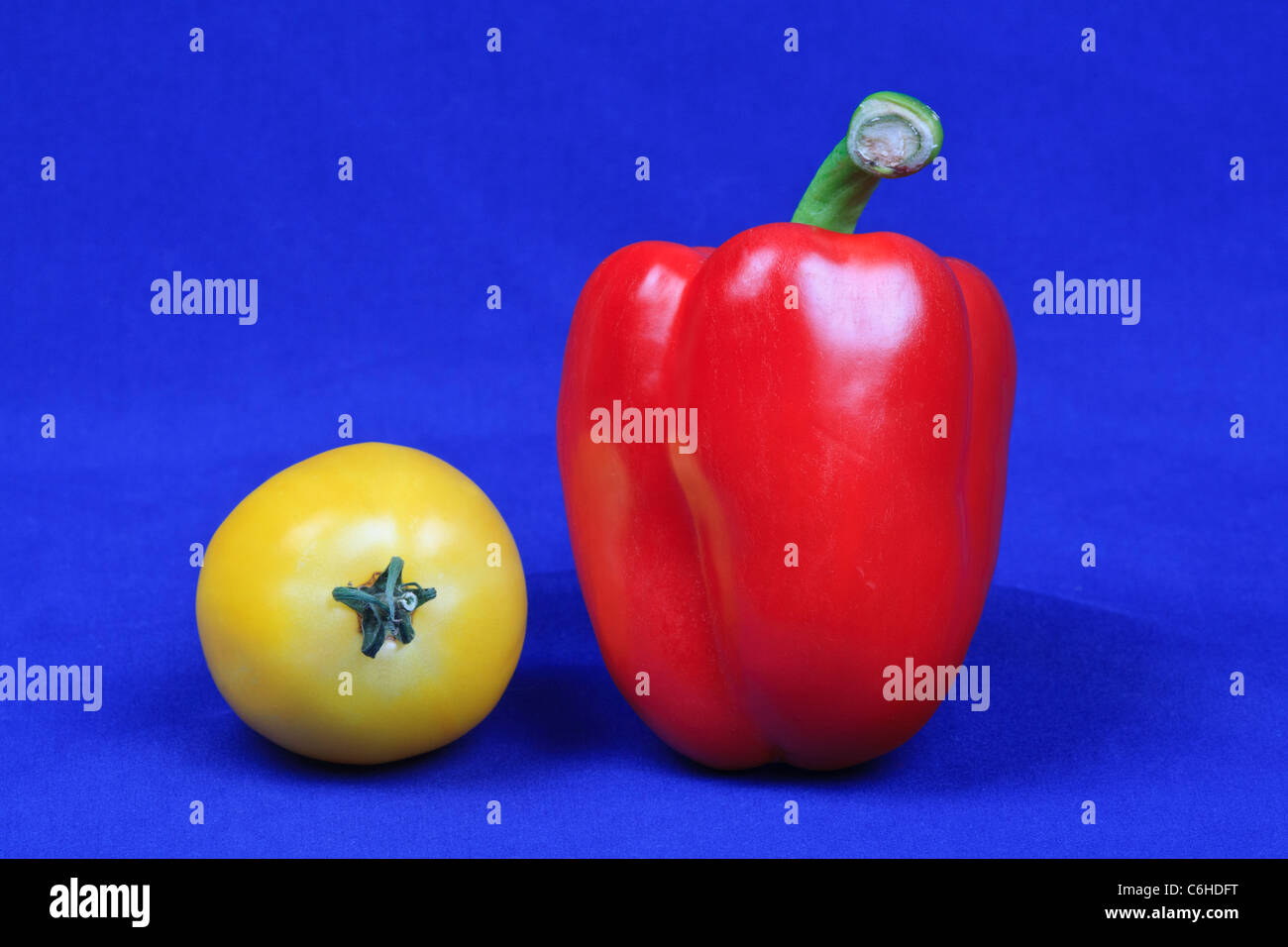Red bell pepper and yellow heritage tomato against a blue background Stock Photo