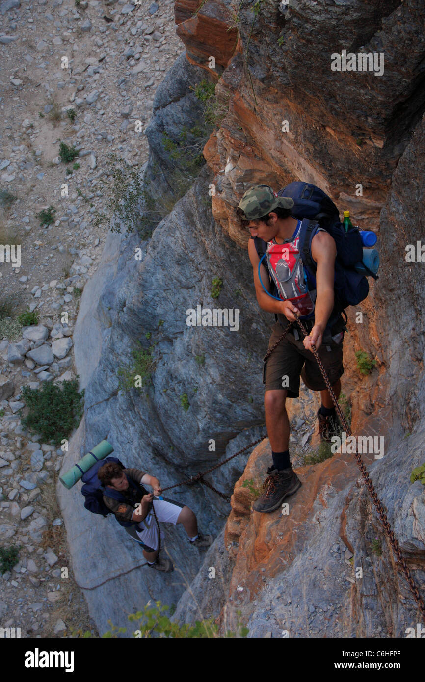 Three hikers descending steep rock face using chains Stock Photo
