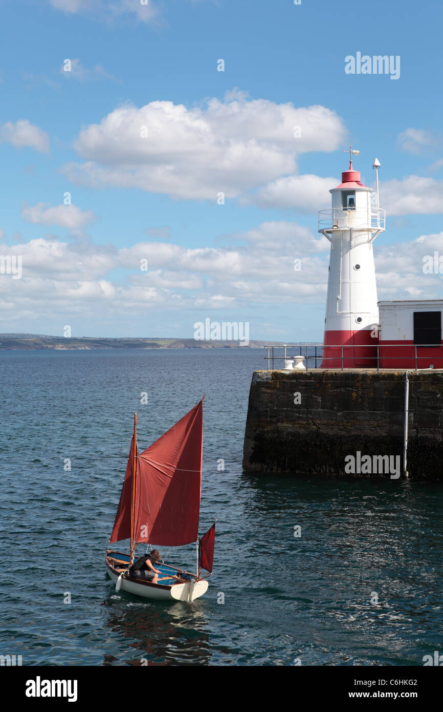 A small sailing boat with a red sail leaves the harbour at Newlyn, Cornwall Stock Photo