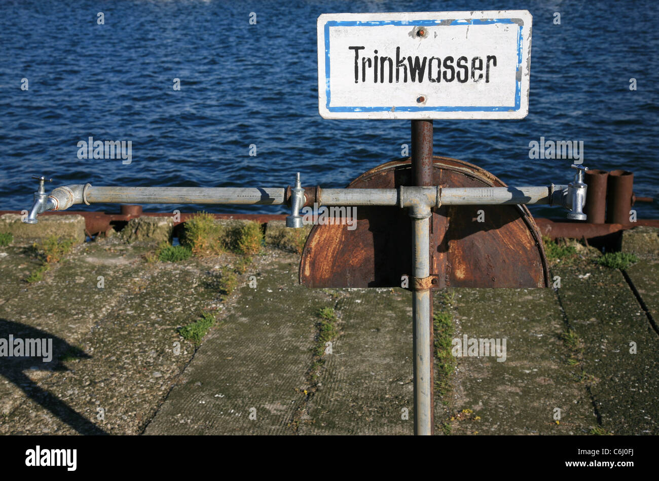Sign with three faucets and water in the background. The German word 'Trinkwasser' on the sign means 'potable water' in English. Stock Photo
