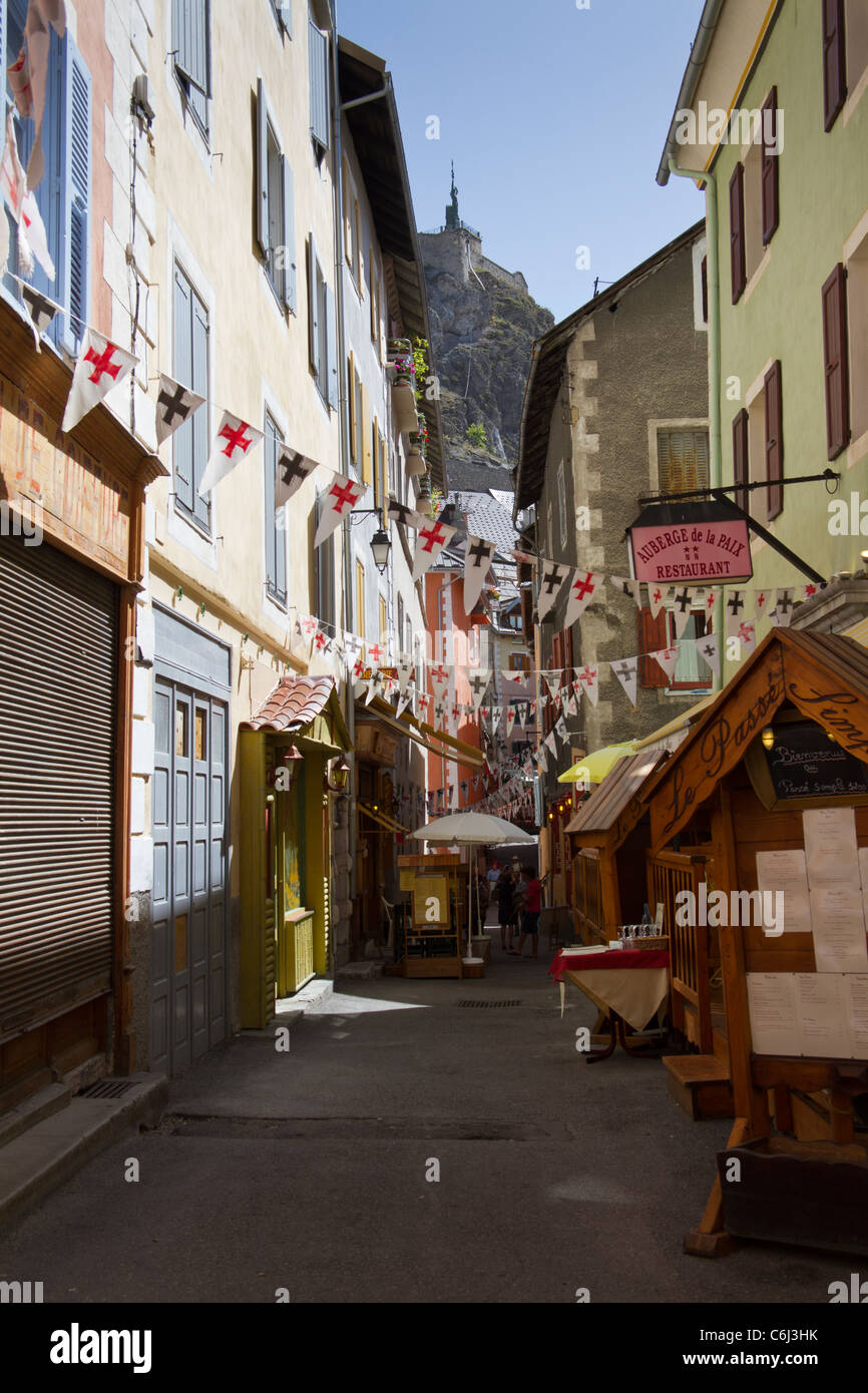 A narrow street with restaurants and bunting in the historic old city of Briançon in summer Stock Photo
