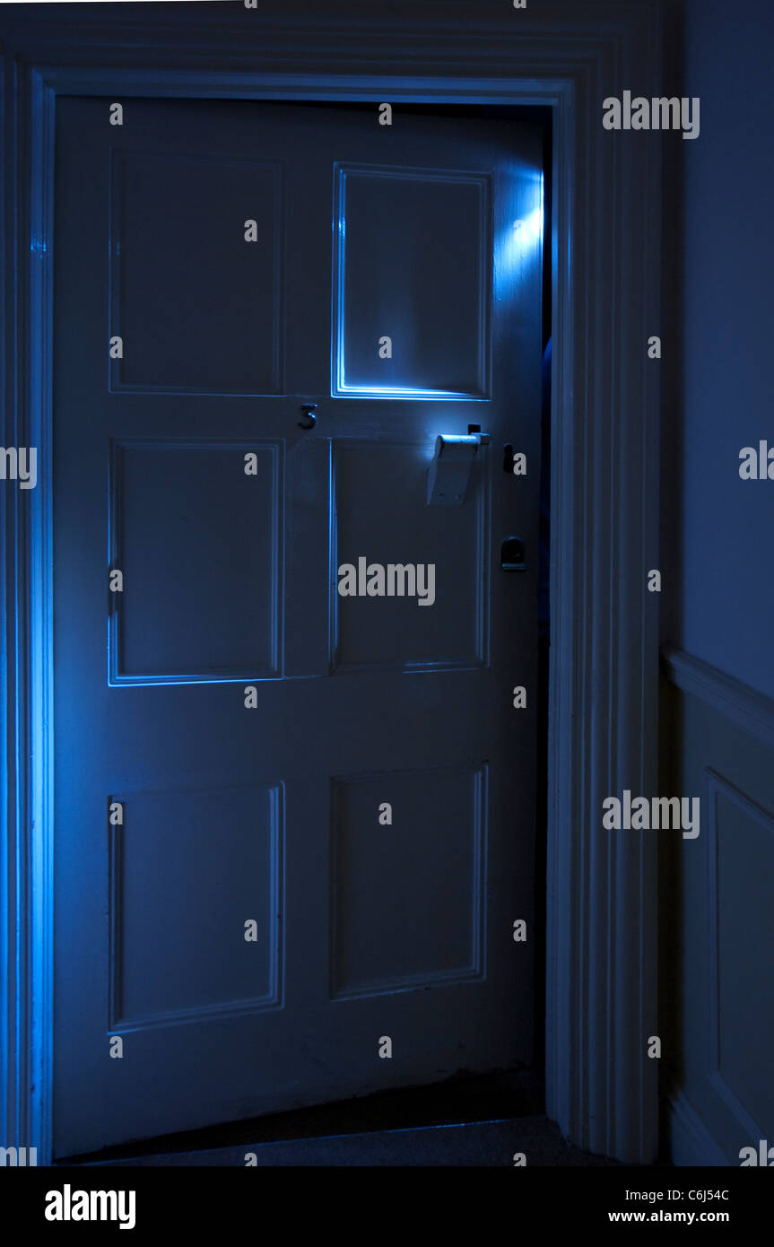 Spooky blue light shining from behind an ajar door Stock Photo