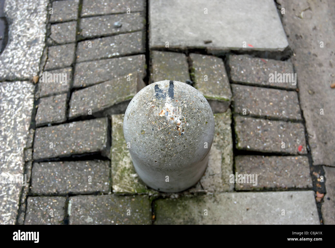 seen from above, a leaning bollard rising from a damaged pavement, in twickenham, middlesex, england Stock Photo