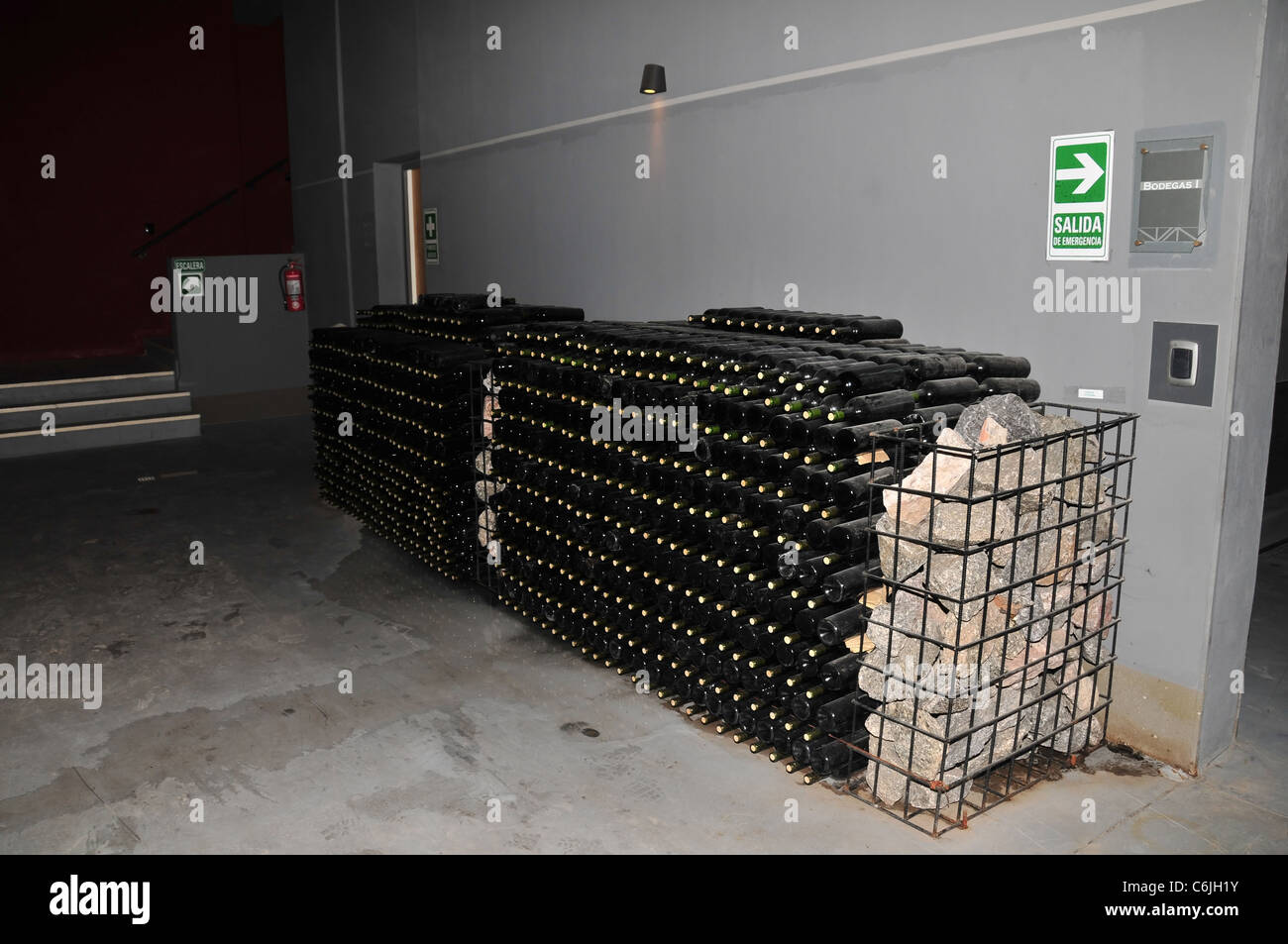 Two large stacks of black wine bottles supported by stone gabions, wine