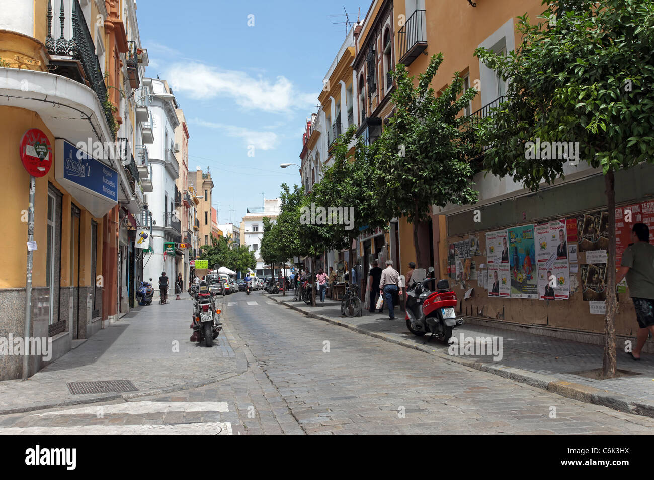 Seville Spain narrow street in old historic part of town. Motorcycles parked on sidewalk as cars drive down cobble stone road. Stock Photo