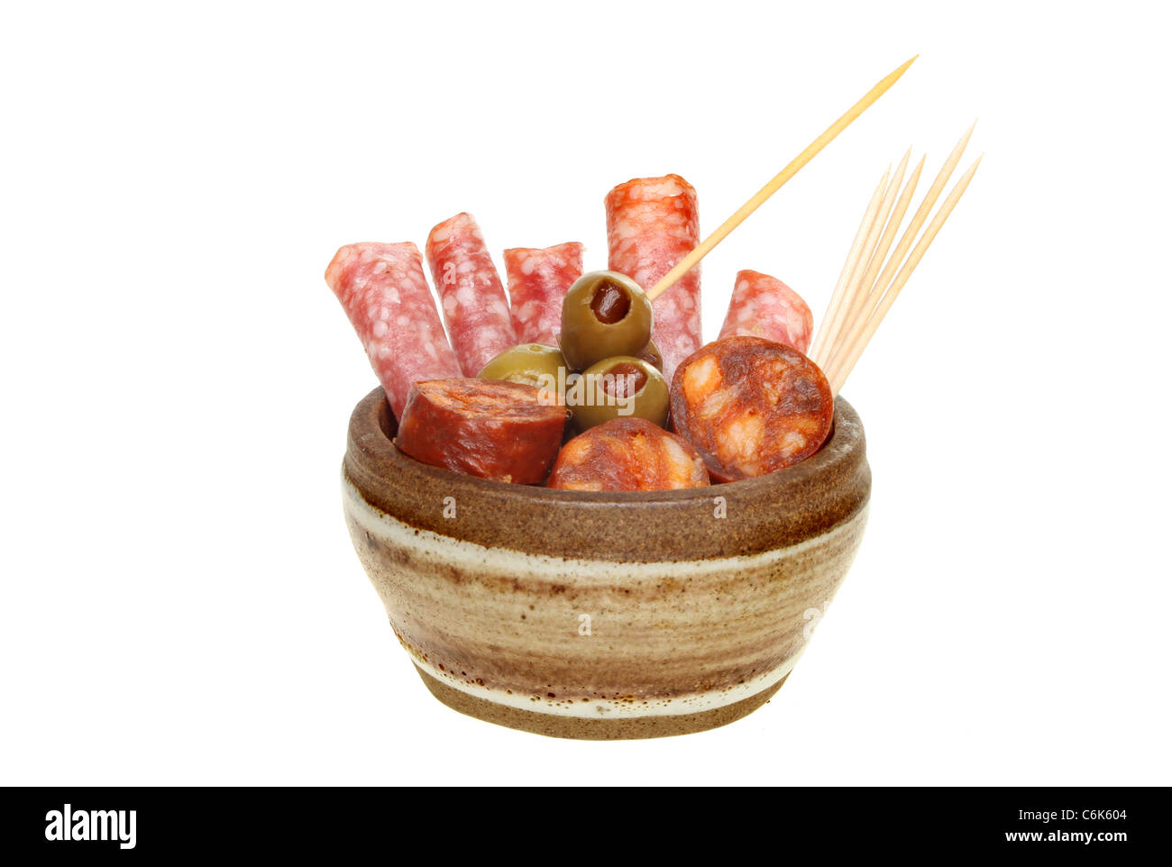 Salami, chorizo sausages and olives in a bowl with cocktail sticks isolated against white Stock Photo