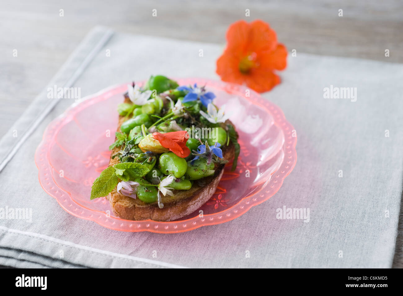 Broad bean and herb tartines with wildflowers Stock Photo